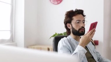 Başarılı genç serbest çalışan adam iş yerinde cep telefonu kullanarak rahatlıyor.