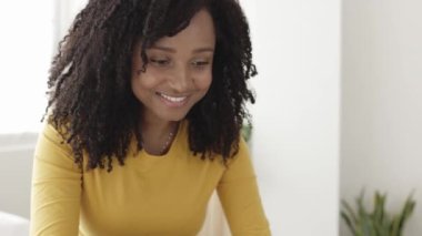 Yatakta dizüstü bilgisayarla çalışan mutlu Afro-Amerikan kadın.