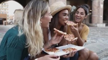 Üç mutlu kadın arkadaş, şehir sokaklarında pizza yiyorlar.