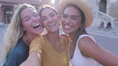 Üç farklı etnik gruptan genç bayan arkadaş birlikte gülüyor dışarıda selfie çekiyorlar.