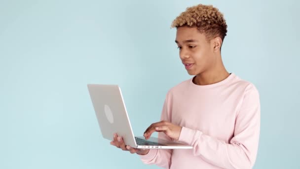 Захоплений підліток святкує хороші новини на ноутбуці на синьому фоні — стокове відео