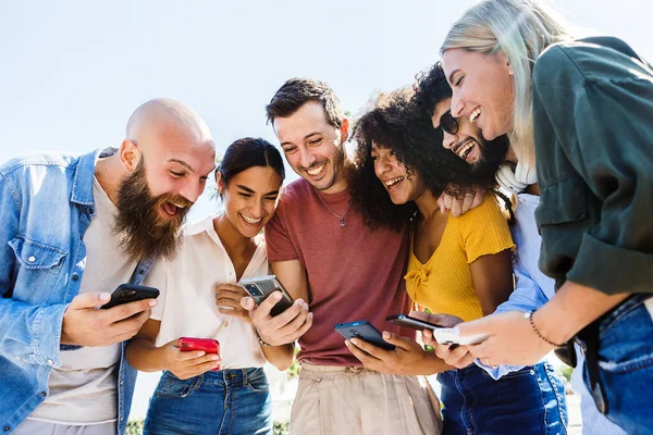 Молода група щасливих людей посміхається під час використання мобільного телефону разом на відкритому повітрі — стокове фото