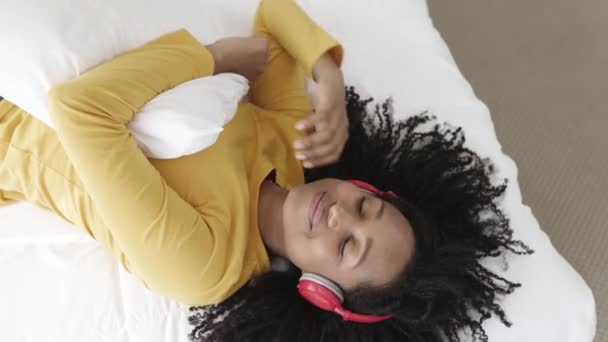 Afrikansk amerikansk kvinna lyssnar på musik som ligger på sängen — Stockvideo