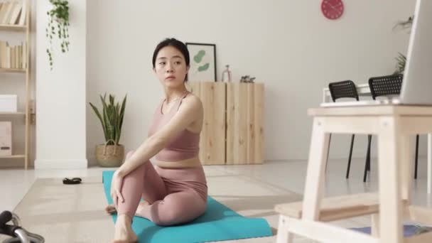 Młoda kobieta siedzi na macie do jogi po zajęciach fitness online na laptopie — Wideo stockowe