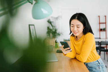 Evde çalışırken cep telefonu kullanan Asyalı genç bir kadın.