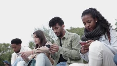 Bir grup genç kız dışarıda otururken akıllı telefonlar kullanıyor.