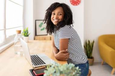 Evde çalışırken kameraya gülümseyen kendinden emin genç Brezilyalı kadın.