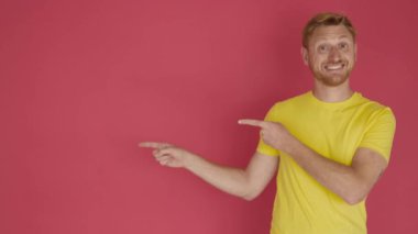 Smiling young adult man pointing with fingers over isolated red background
