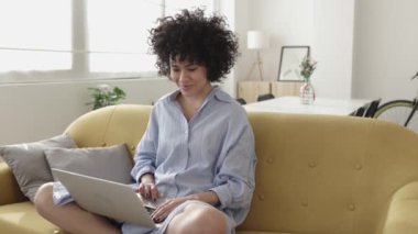 Evde dizüstü bilgisayar kullanan genç bir kadın. 