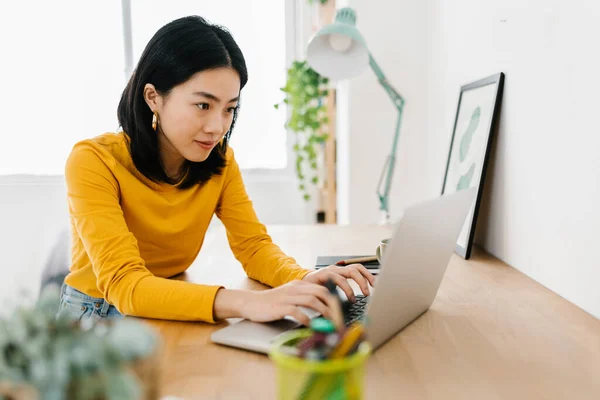 Joven mujer asiática usando un ordenador portátil mientras estudia en línea desde casa. — Foto de Stock