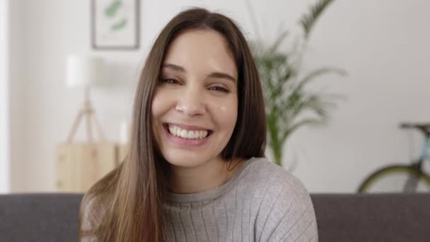 Молода дружня біла жінка посміхається на камеру, розслабляючись вдома — стокове відео
