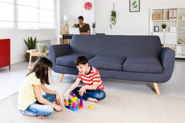 Babaları evde dizüstü bilgisayarıyla uğraşırken iki küçük çocuk birlikte oynuyor.