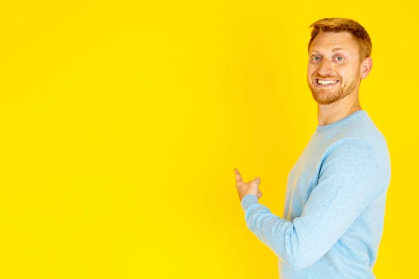 Jovem alegre apontando para trás com o dedo no espaço cópia fundo amarelo — Fotografia de Stock