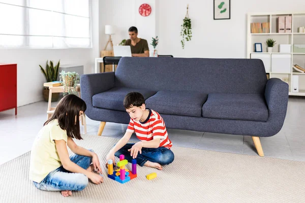 Babaları evde dizüstü bilgisayarıyla uğraşırken iki küçük çocuk birlikte oynuyor.