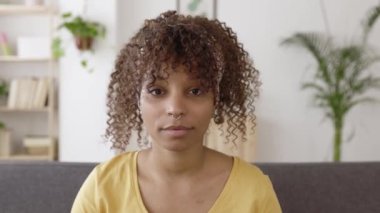 Young african american woman smiling at camera while sitting on sofa at home