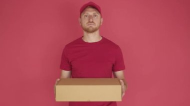 Isolated delivery man holding cardboard box over red background