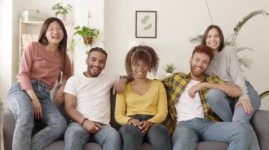 Group portrait of smiling diverse young people sitting on sofa looking at camera