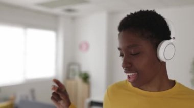 Kulaklıkla müzik dinlerken dans eden mutlu Afrikalı genç bir kadın.