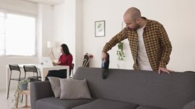 Kanepeyi elektrikli süpürgeyle temizleyen genç bir adam.
