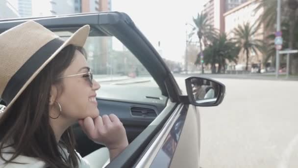 Pretty woman looking out while sitting on cabriolet car in city street — Video