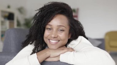 Evdeki kanepede uzanmış kameraya gülümseyen mutlu genç Brezilyalı kadın.