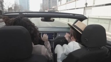 Happy young couple listening to music while driving cabriolet car in the city