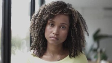 Brezilya 'lı kıvırcık saçlı genç kadın pencereye yakın kameraya bakıyor.