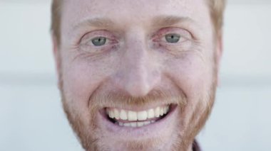 Kameraya gülümseyen kızıl saçlı genç adamın yakın portresi.