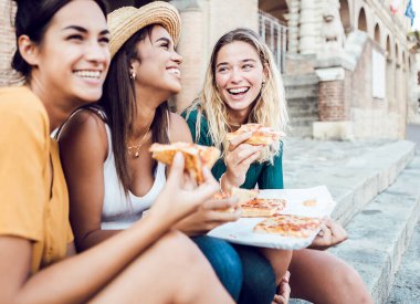 İtalyan pizzası yiyen mutlu genç kadın turistler yaz tatilinin tadını çıkarıyorlar.
