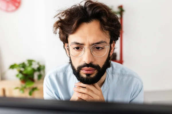 Hombre barbudo joven en gafas de trabajo concentrado en el ordenador portátil desde casa — Foto de Stock