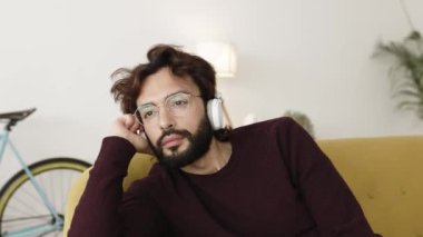 Genç adam evde oturup kulaklıkla müzik dinliyor.