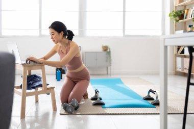 Genç Asyalı kadın evde dizüstü bilgisayarda sanal fitness dersi arıyor.