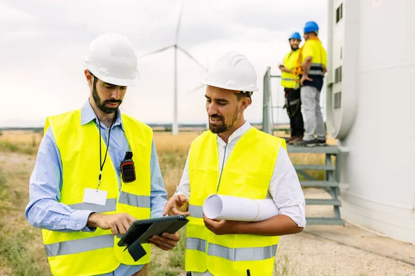 Two young maintenance engineers team working in wind turbine farm - Professional technicians males of maintenance control discussing about power station construction site