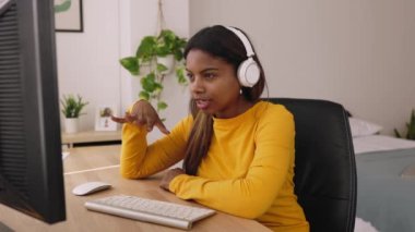 Latin kökenli genç bir kadın odasında internetten ders çalışıyor. Genç kız el sallıyor ve dizüstü bilgisayarında video görüşmesi yapıyor - Eğitim ve çevrimiçi öğrenim kavramı