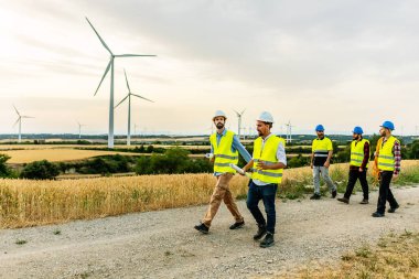Bir grup teknisyen ve mühendis rüzgar tarlasında yürüyorlar - yenilenebilir ve alternatif enerji kavramı