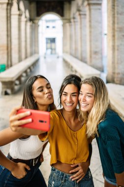 İtalya 'da yaz tatili sırasında cep telefonuyla selfie çeken çok ırklı en iyi kadın arkadaş grubunun dikey çekimi - seyahat ve kadın arkadaşlık kavramı