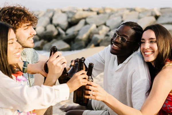 Best friends celebrating together at summer vacation - Multiracial young people having fun while cheering with beer bottles relaxing at beach