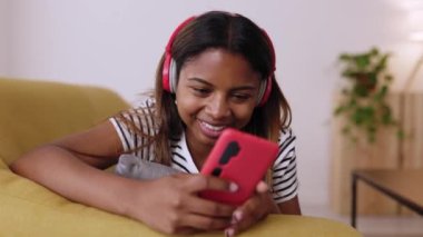 Gülümseyen Latin genç kız koltukta dinleniyor cep telefonu kullanıyor genç kadın akıllı cep telefonuyla komik videolar izlerken eğleniyor boş zaman ve teknoloji konsepti 