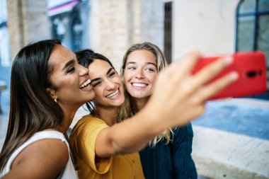 Young happy woman friends of different ethnicities having fun taking selfie portrait outdoor
