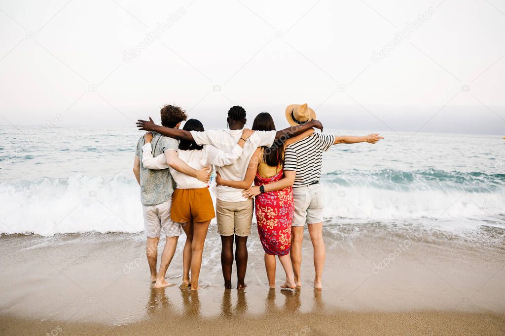 Group of young people hugging each other and enjoying summer at beach