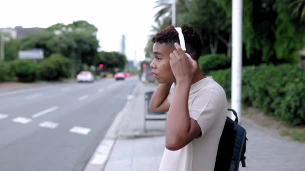 Młody Nastolatek Wkładający Słuchawki Słuchania Muzyki Podczas Spaceru Ulicą Miasta — Wideo stockowe