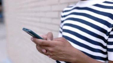 Closeup young african american man using mobile phone outdoor - Millennial guy hands chatting on smartphone while leaning on wall