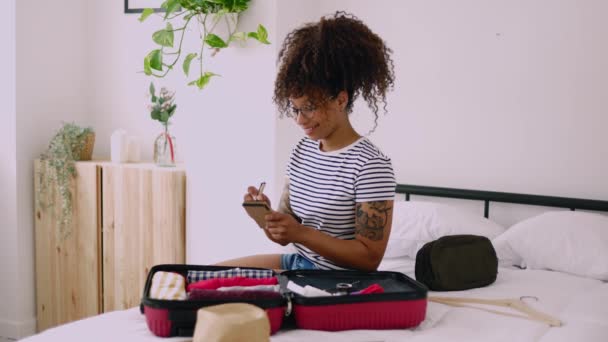 Young African American Woman Packing Clothes Suitcase Writing Travel Checklist — Vídeo de Stock