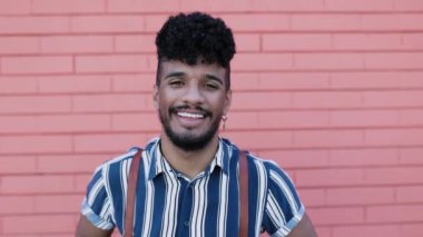 Face portrait of cheerful young hispanic latin man smiling at camera against brick wall outdoor. Happy people concept. High quality 4k footage