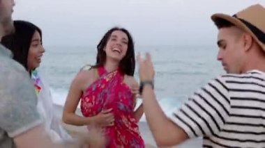 Happy young group of multiracial people dancing at beach party in summer holiday. Millennial diverse friends having fun celebrating on vacation. Friendship and celebration concept.
