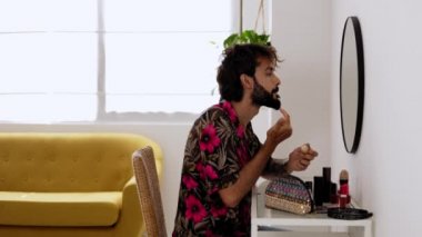 Young adult man putting lip cream in front of the mirror in room at home. Homosexual gay taking care of his facial skin. Skin care treatment and LGTBI people concept. High quality 4k footage