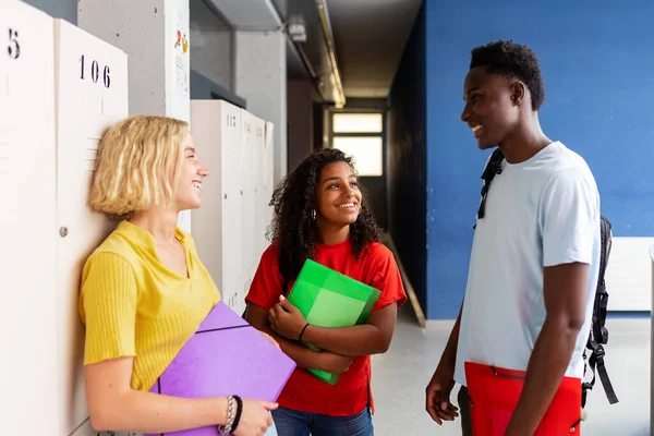 Multiracial group of student friends talking at high school corridor - Millennial young people having a conversation at college after classroom - Youth lifestyle, education and community concept