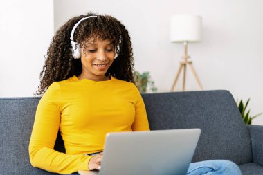 Cheerful afro american freelancer woman using laptop on sofa