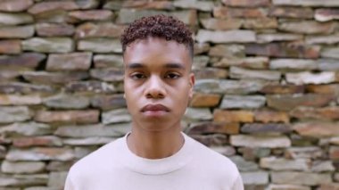 Young teenage boy looking serious at camera outdoor. Face portrait of confident millennial hispanic latin guy standing in city street. High quality 4k footage