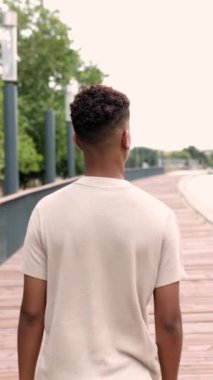 Vertical back view footage of unrecognizable hispanic latino teenager boy walking alone outdoor in city street. Slow motion high quality HD video. Youth, success and confidence concept
